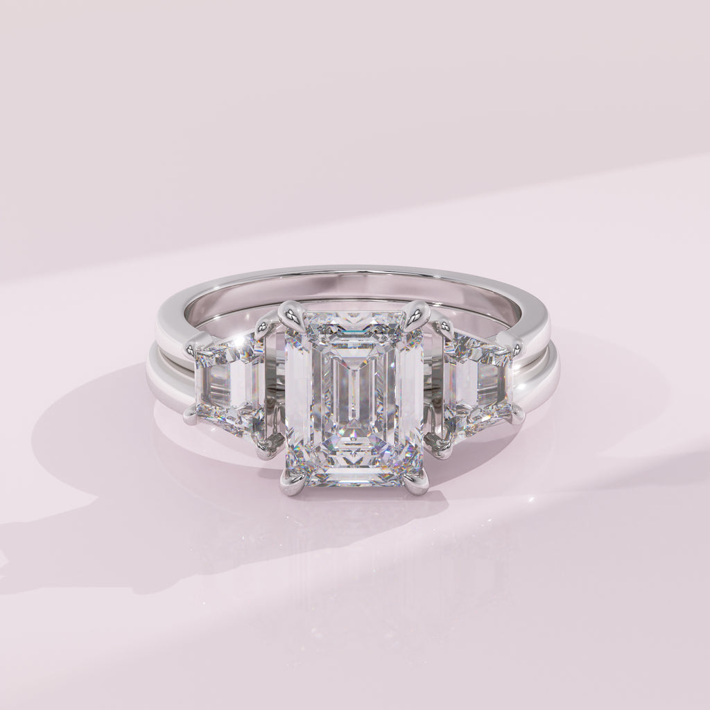 Diamond ring with emerald-cut center stone and baguette side stones on a light pink background