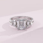 Diamond ring with emerald-cut center stone and baguette side stones on a light pink background
