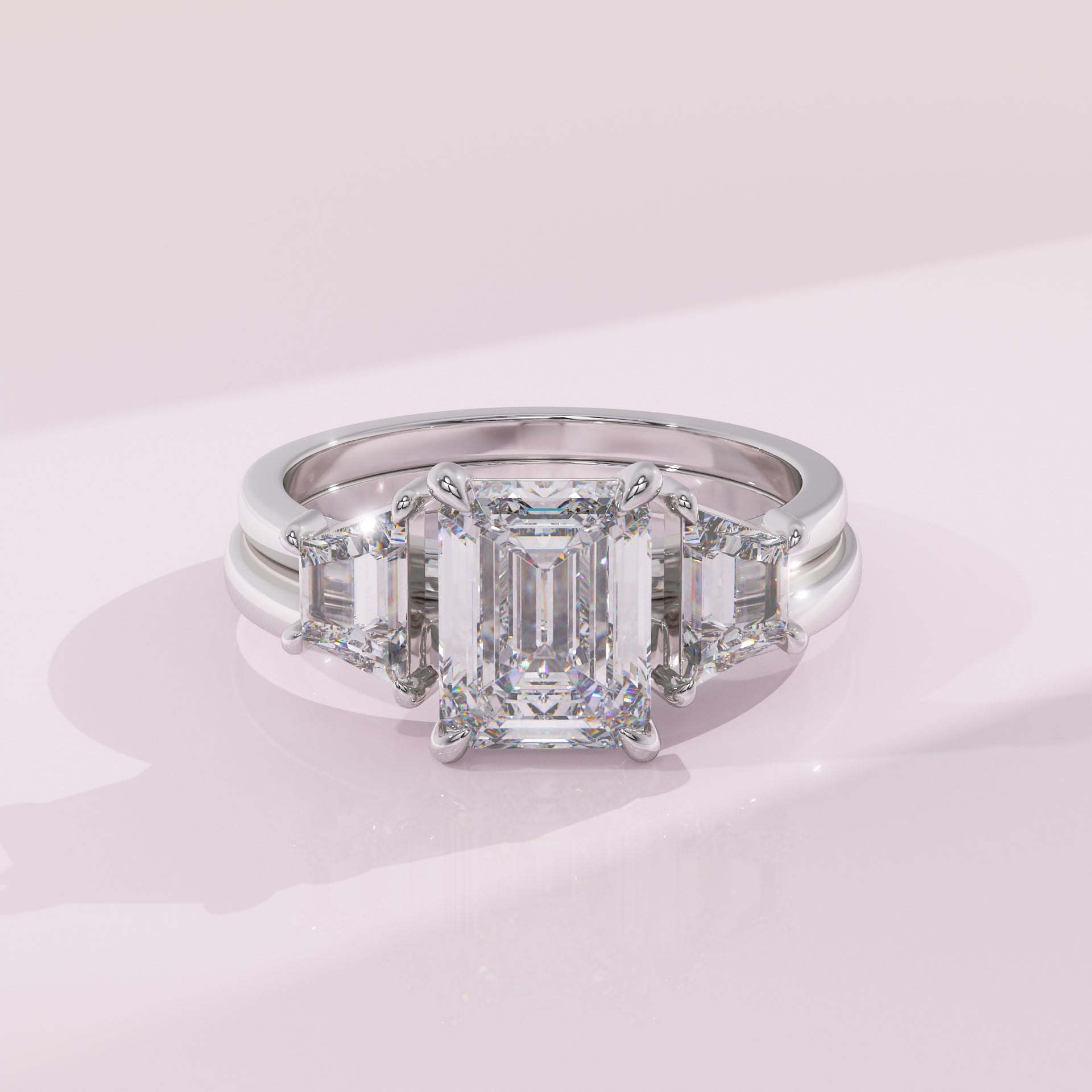 Diamond ring with emerald-cut center stone and baguette side stones on a light pink background