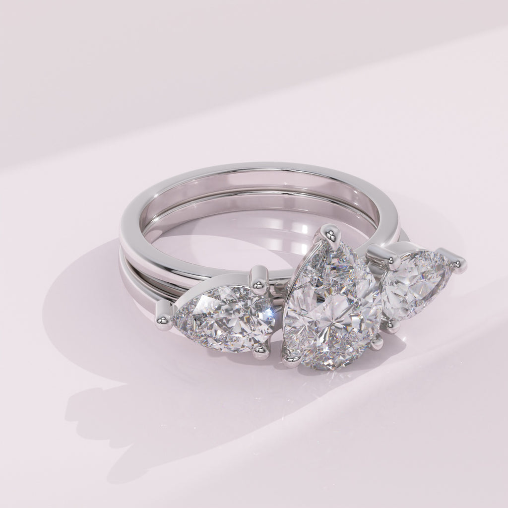 Silver ring with pear-shaped diamonds on a light pink background